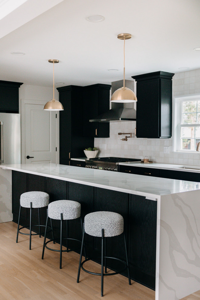Midcentury kitchen in Detroit with a drop-in sink, flat-panel cabinets, black cabinets, quartzite benchtops, white splashback, ceramic splashback, stainless steel appliances, medium hardwood floors, with island, brown floor and white benchtop.