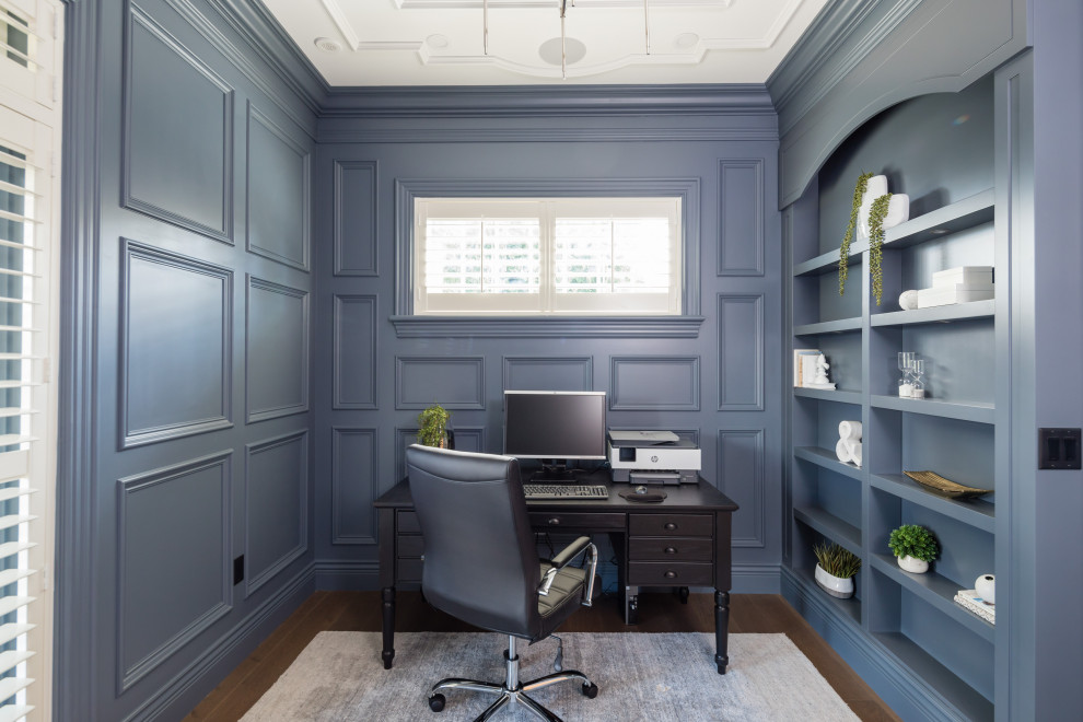 Traditional study room in Other with blue walls, medium hardwood floors, no fireplace, a freestanding desk, brown floor and panelled walls.
