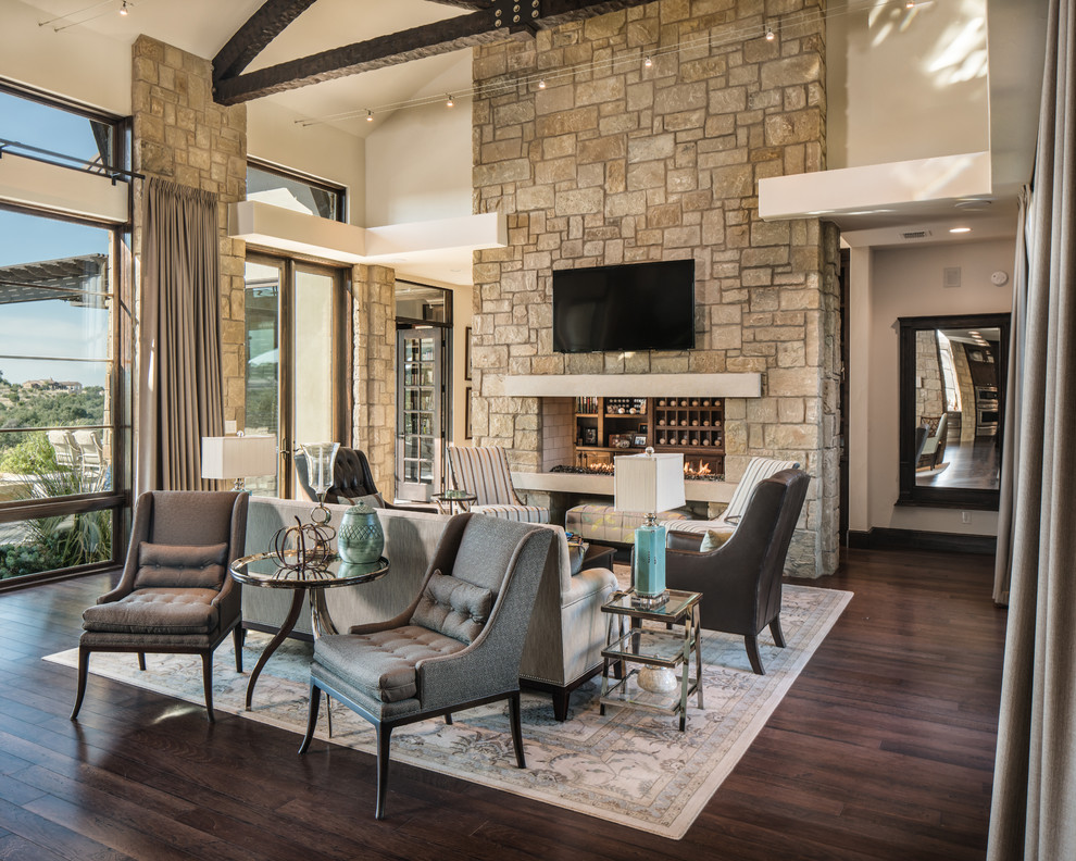 This is an example of a large mediterranean open concept living room in Austin with beige walls, dark hardwood floors, a two-sided fireplace, a stone fireplace surround, a wall-mounted tv and brown floor.