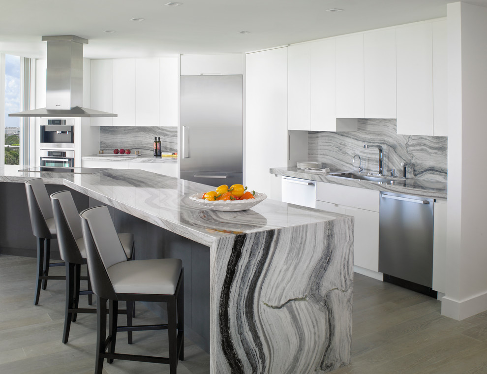 Photo of a contemporary kitchen in Miami with a single-bowl sink, flat-panel cabinets, white cabinets, grey splashback, stainless steel appliances and with island.