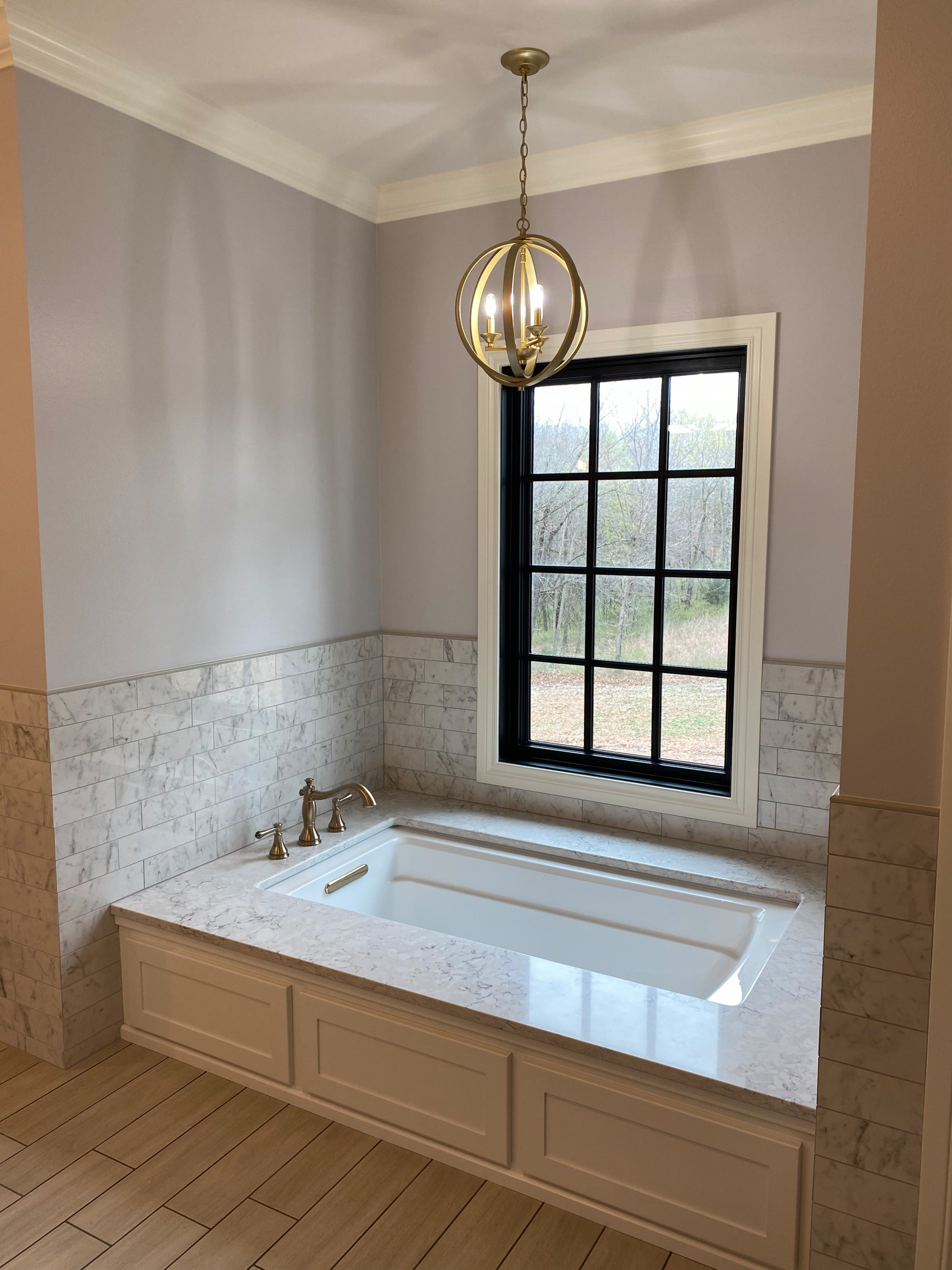 Master bathtub with quartz surround, tile backsplash, and champagne bronze light