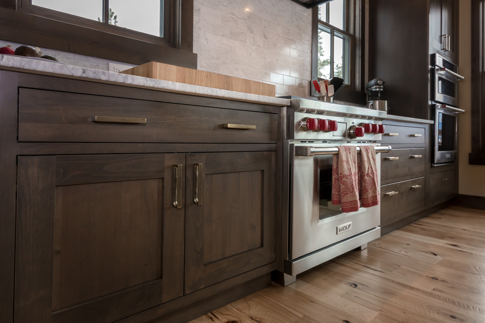 Open concept kitchen - large rustic l-shaped light wood floor and beige floor open concept kitchen idea in Denver with an undermount sink, shaker cabinets, dark wood cabinets, quartz countertops, beige backsplash, subway tile backsplash, stainless steel appliances, an island and white countertops