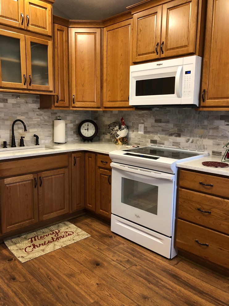 Mid-sized transitional u-shaped laminate floor and brown floor eat-in kitchen photo in Omaha with an undermount sink, raised-panel cabinets, medium tone wood cabinets, quartz countertops, beige backsplash, stone tile backsplash, white appliances and white countertops