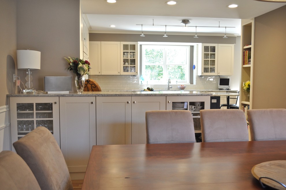 Example of a mid-sized transitional l-shaped light wood floor and brown floor enclosed kitchen design in Denver with a farmhouse sink, shaker cabinets, white cabinets, marble countertops, white backsplash, ceramic backsplash, stainless steel appliances and an island