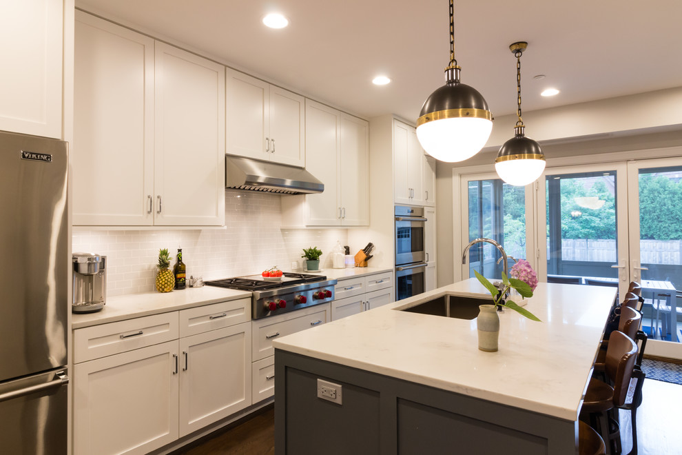 Photo of a transitional eat-in kitchen in Boston with an undermount sink, shaker cabinets, white cabinets, marble benchtops, grey splashback, subway tile splashback, stainless steel appliances, dark hardwood floors, with island and brown floor.
