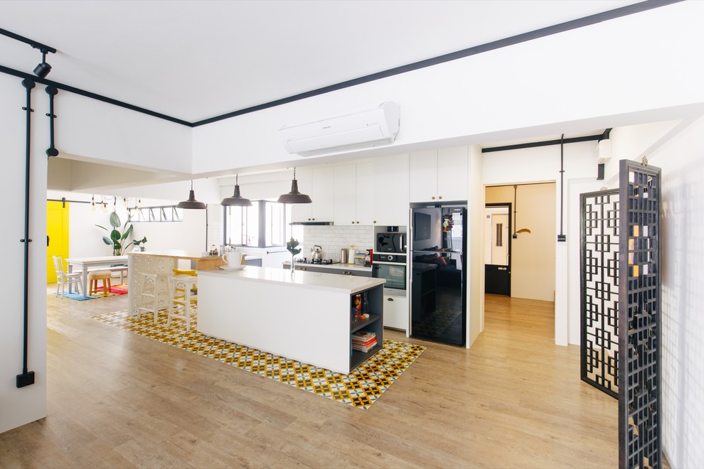 Design ideas for an eclectic galley eat-in kitchen in Singapore with white cabinets, white splashback, black appliances, light hardwood floors, with island, brown floor and white benchtop.