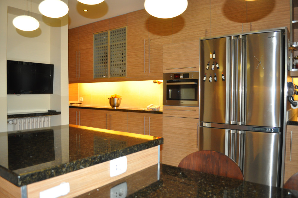 Enclosed kitchen - mid-sized modern galley ceramic tile and beige floor enclosed kitchen idea with flat-panel cabinets, medium tone wood cabinets, granite countertops, beige backsplash, ceramic backsplash, stainless steel appliances, an island, black countertops and a double-bowl sink