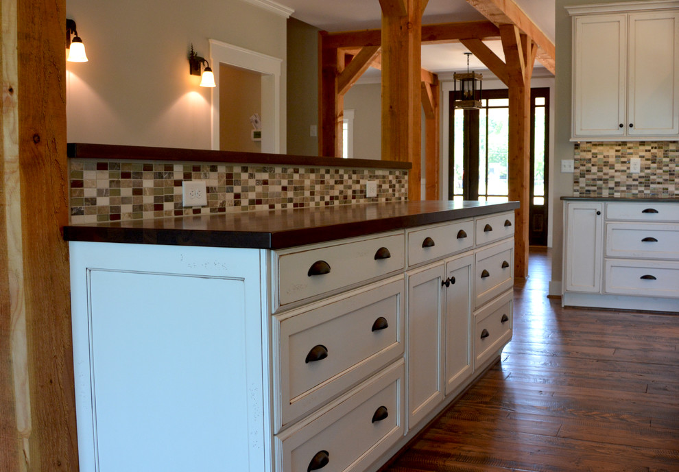 Example of a large mountain style dark wood floor eat-in kitchen design with an undermount sink, recessed-panel cabinets, distressed cabinets, granite countertops, multicolored backsplash, glass tile backsplash, stainless steel appliances and an island