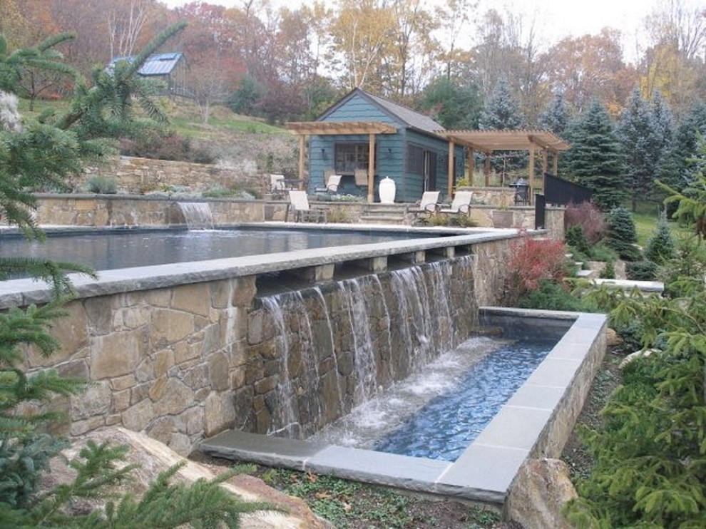 This is an example of a mid-sized country backyard rectangular pool in Bridgeport with a water feature and natural stone pavers.