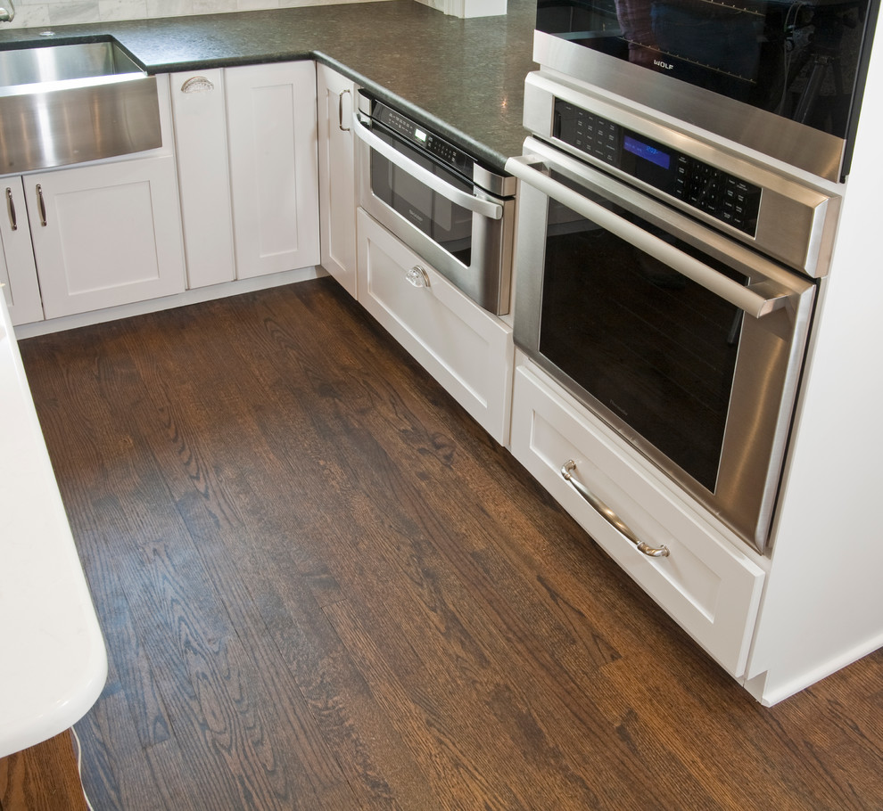 Inspiration for a large transitional l-shaped medium tone wood floor eat-in kitchen remodel in Philadelphia with a farmhouse sink, shaker cabinets, white cabinets, granite countertops, gray backsplash, stone tile backsplash, stainless steel appliances and an island