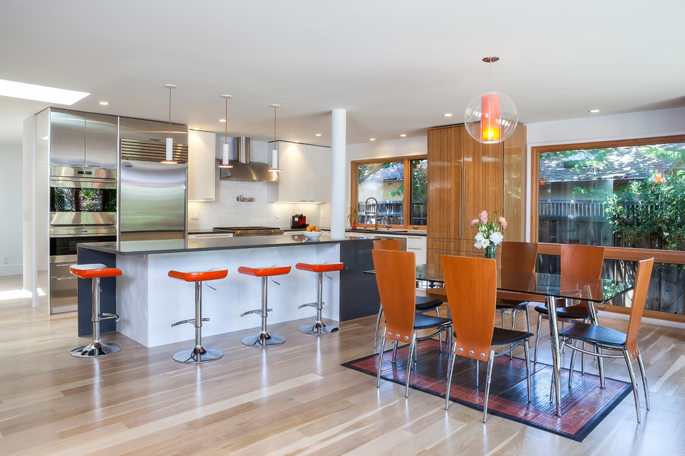 This is an example of a large contemporary l-shaped eat-in kitchen in San Francisco with flat-panel cabinets, white cabinets, quartz benchtops, white splashback, porcelain splashback, stainless steel appliances, with island, an undermount sink, light hardwood floors and beige floor.