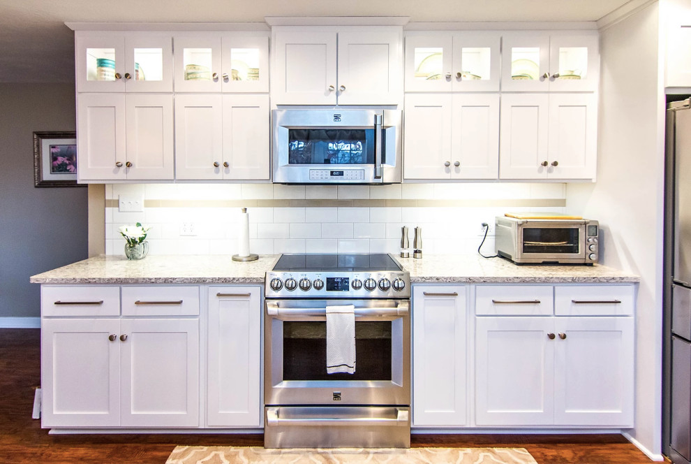 Example of a large transitional galley medium tone wood floor and brown floor enclosed kitchen design with an undermount sink, white cabinets, quartzite countertops, white backsplash, stainless steel appliances, shaker cabinets, ceramic backsplash, a peninsula and multicolored countertops