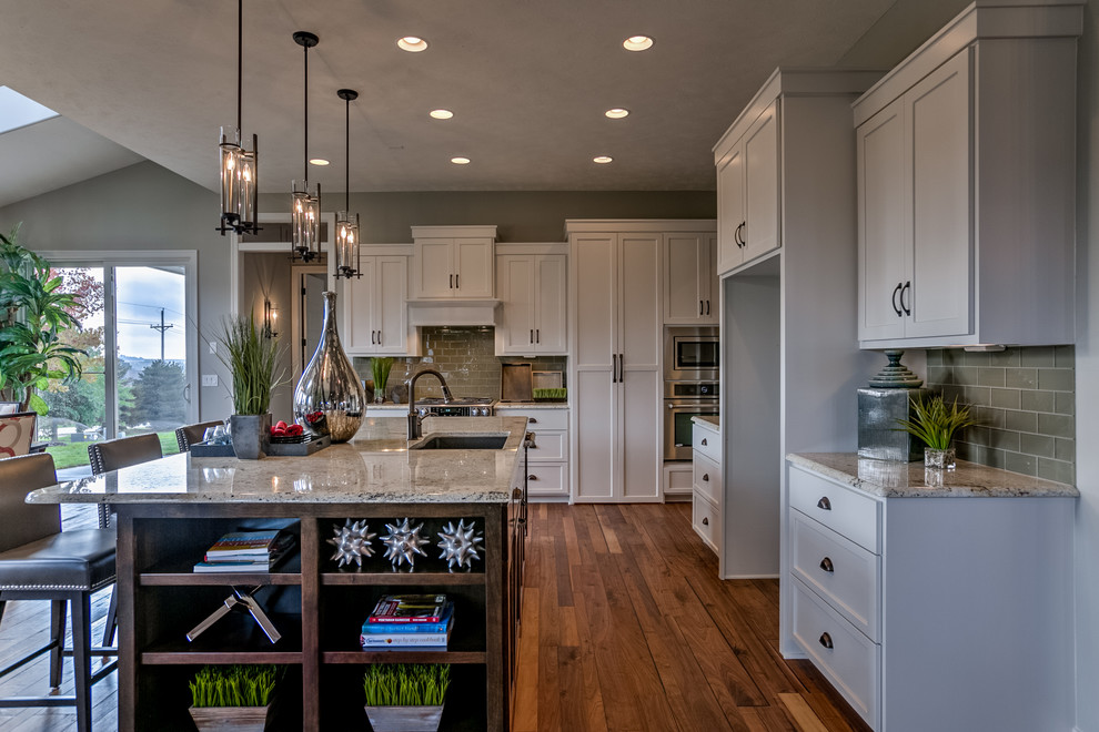 Design ideas for a transitional l-shaped open plan kitchen in Omaha with an undermount sink, shaker cabinets, white cabinets, green splashback, glass tile splashback, stainless steel appliances, dark hardwood floors and with island.
