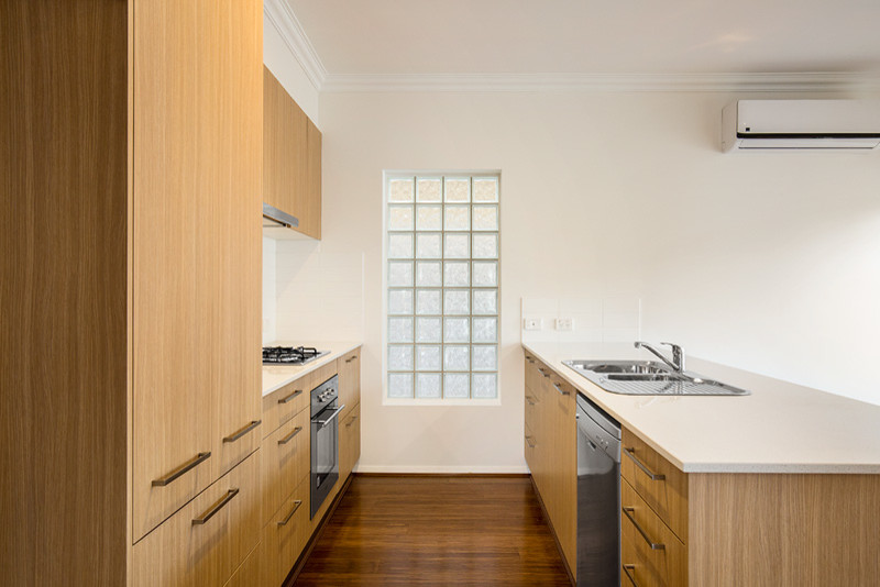 This is an example of a mid-sized traditional u-shaped separate kitchen in Melbourne with a double-bowl sink, flat-panel cabinets, medium wood cabinets, quartz benchtops, white splashback, ceramic splashback, stainless steel appliances, vinyl floors, with island and brown floor.