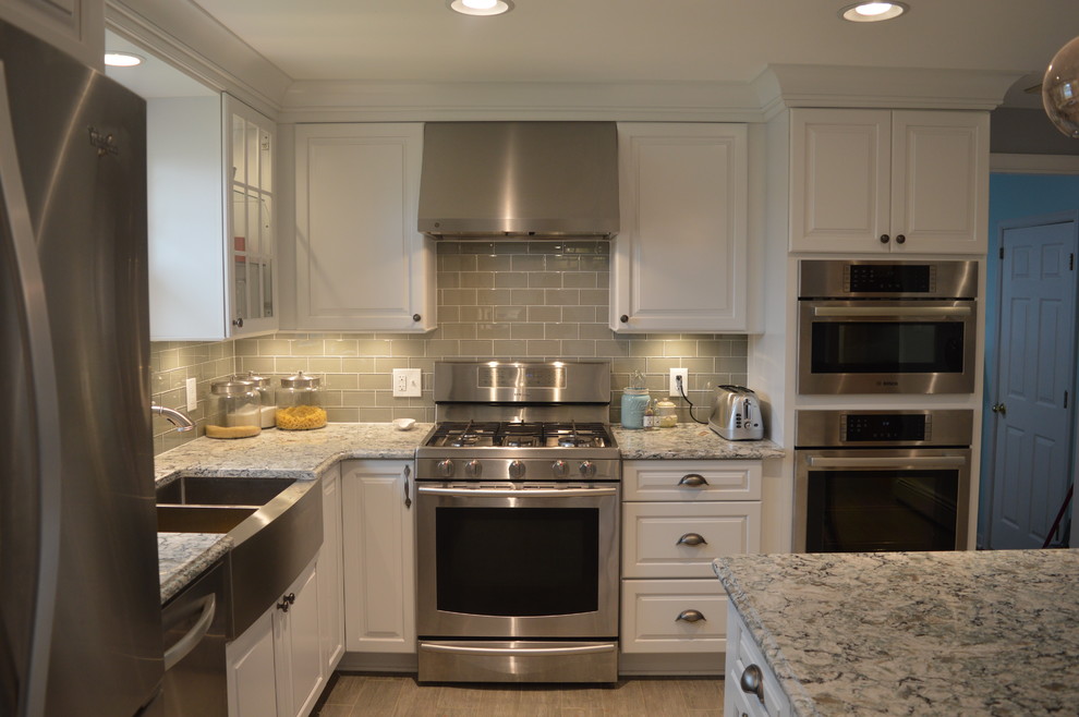 Large transitional u-shaped ceramic tile and gray floor enclosed kitchen photo with a farmhouse sink, raised-panel cabinets, white cabinets, quartz countertops, gray backsplash, glass tile backsplash, stainless steel appliances and an island
