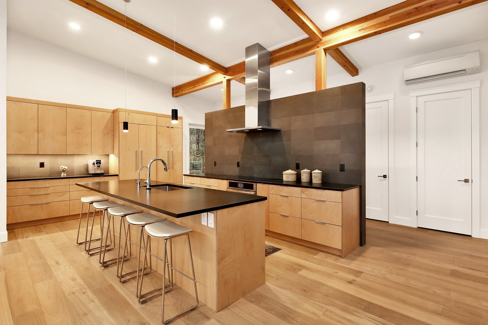 Photo of a large contemporary single-wall eat-in kitchen in Seattle with a drop-in sink, flat-panel cabinets, light wood cabinets, granite benchtops, black splashback, stone tile splashback, stainless steel appliances, light hardwood floors, with island, brown floor and black benchtop.