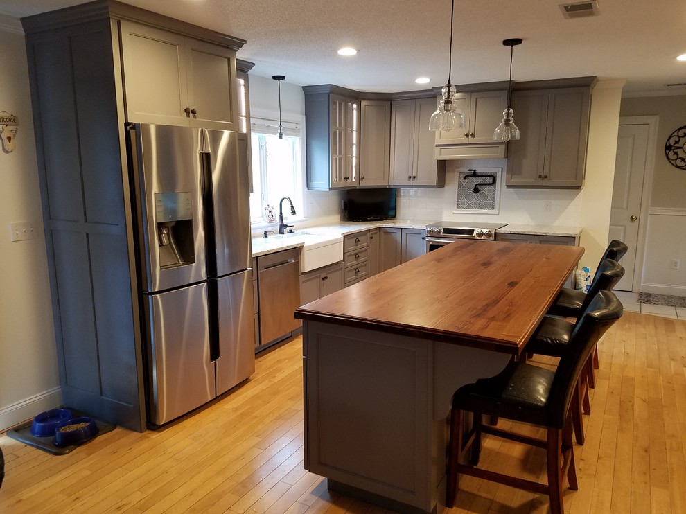 Mid-sized transitional galley light wood floor and brown floor eat-in kitchen photo with a farmhouse sink, recessed-panel cabinets, gray cabinets, wood countertops, white backsplash, subway tile backsplash, stainless steel appliances and an island