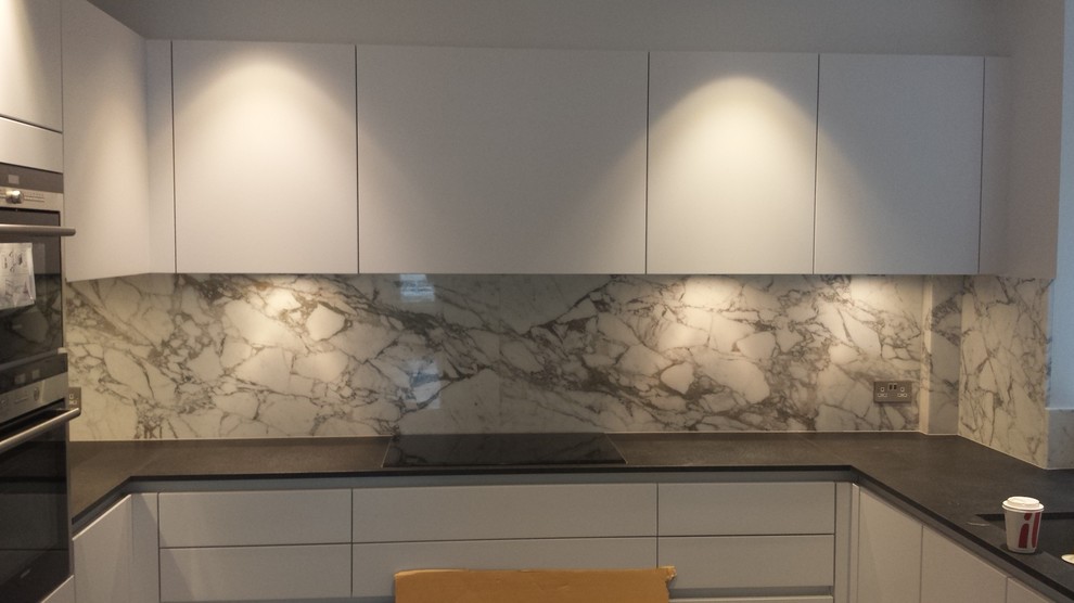 Inspiration for a mid-sized contemporary u-shaped eat-in kitchen in London with flat-panel cabinets, white cabinets, granite benchtops, white splashback, stone tile splashback and no island.