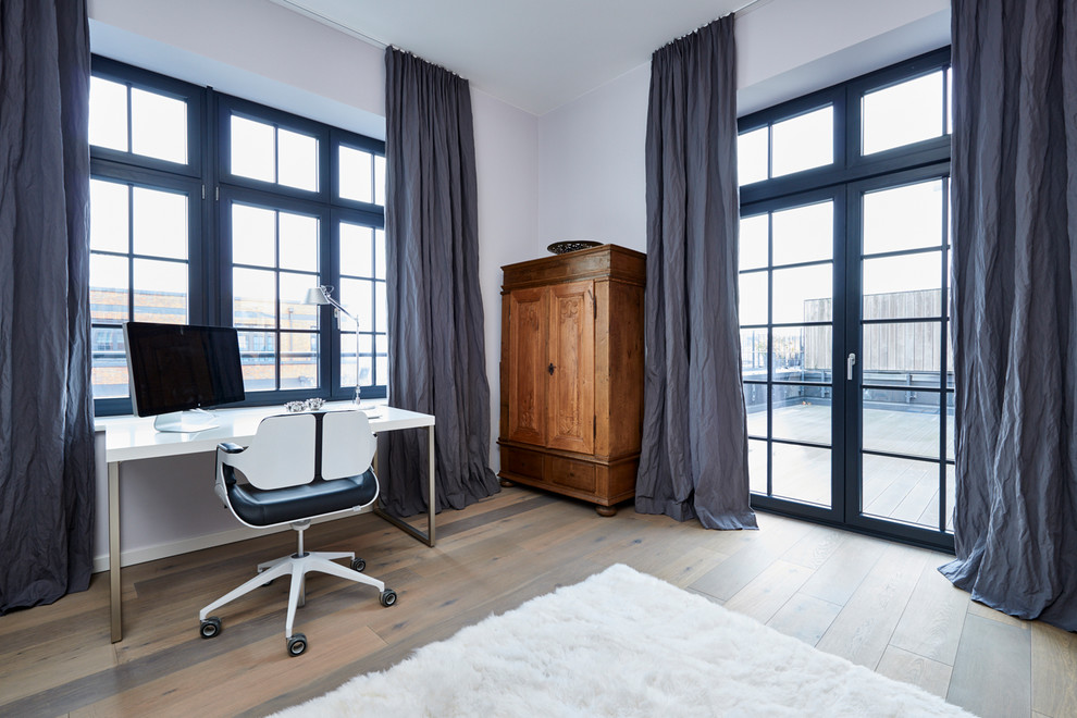 This is an example of a large contemporary home office in Hamburg with a library, grey walls, medium hardwood floors, a freestanding desk and brown floor.