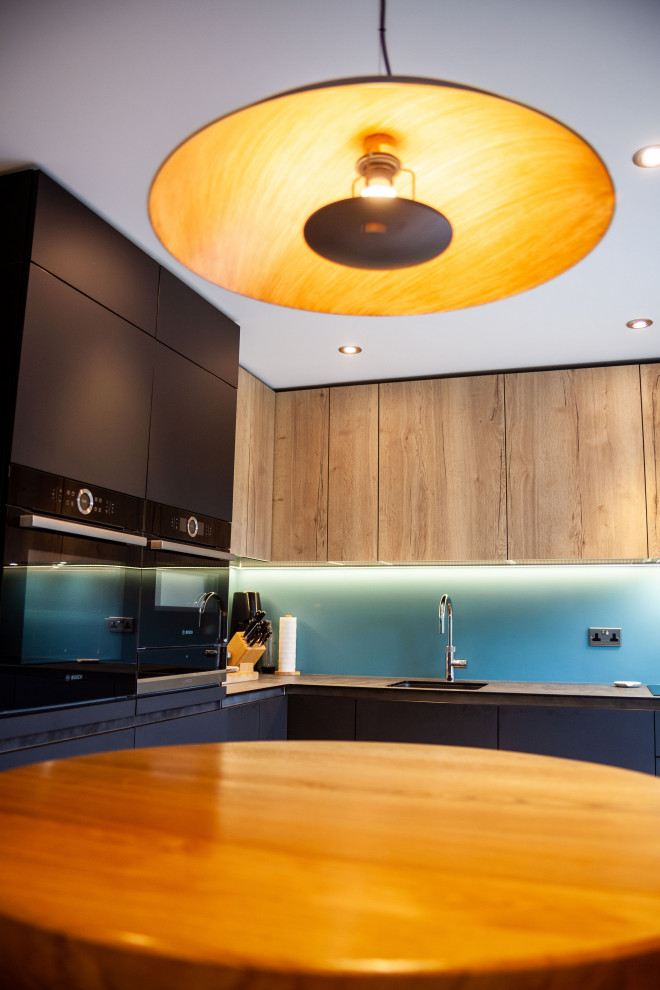 Inspiration för mellanstora moderna kök med öppen planlösning, med en enkel diskho, släta luckor, blått stänkskydd, glaspanel som stänkskydd och svarta vitvaror