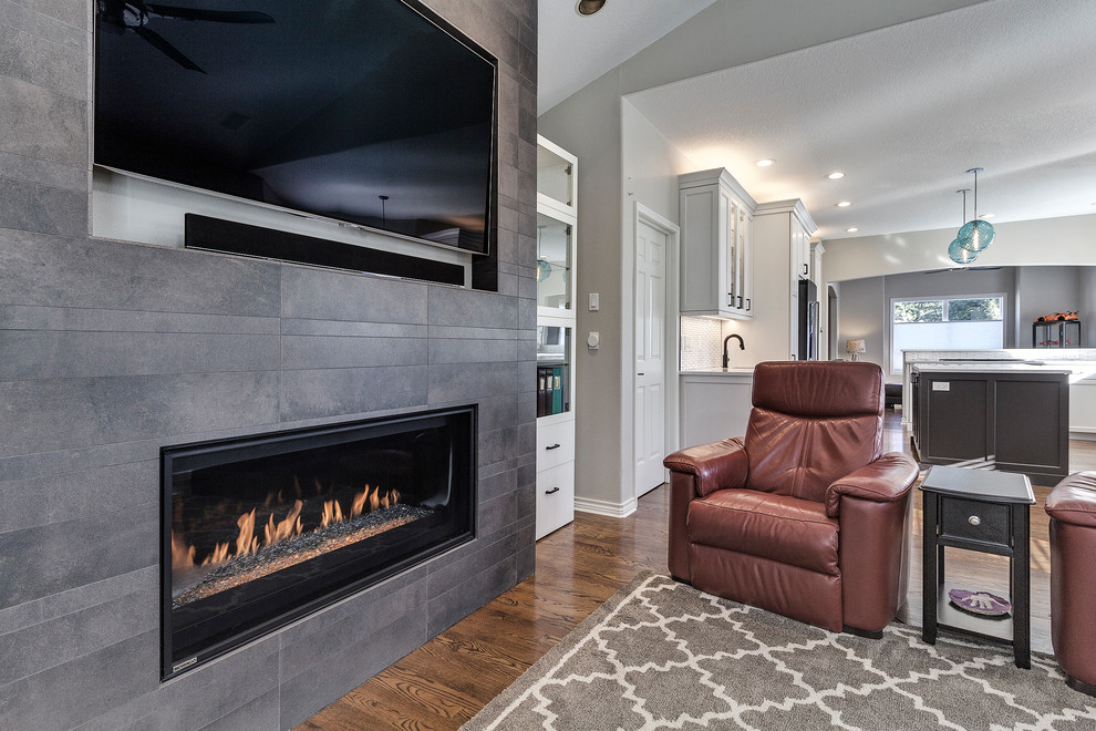 Inspiration for a mid-sized modern open concept family room in Portland with grey walls, dark hardwood floors, a standard fireplace, a tile fireplace surround, a wall-mounted tv and brown floor.
