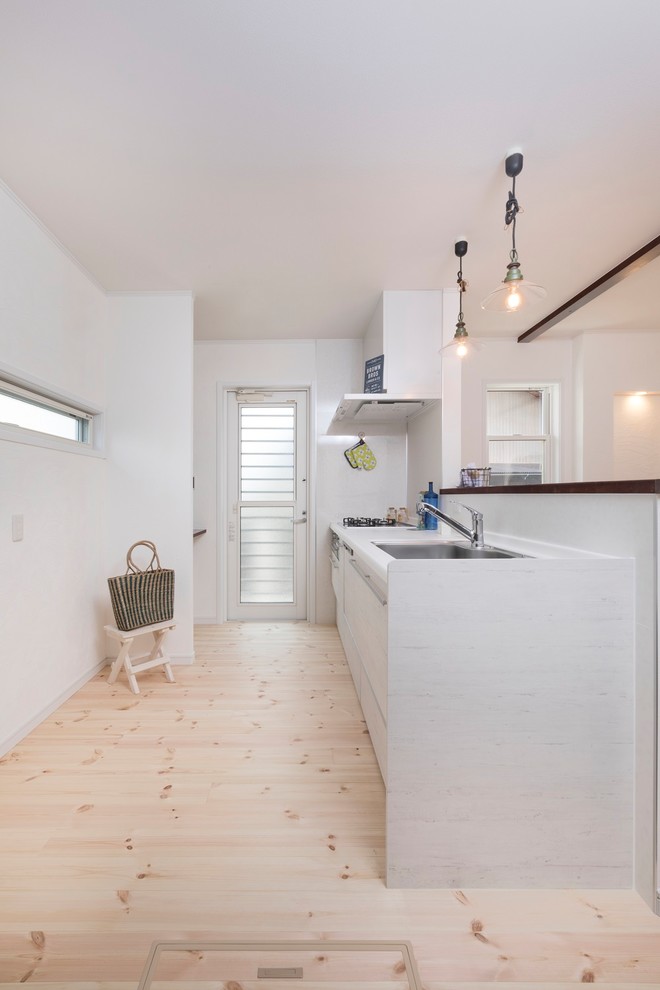 This is an example of a country single-wall open plan kitchen in Other with a single-bowl sink, white cabinets, solid surface benchtops, white splashback, black appliances, light hardwood floors, with island, white floor, flat-panel cabinets and white benchtop.