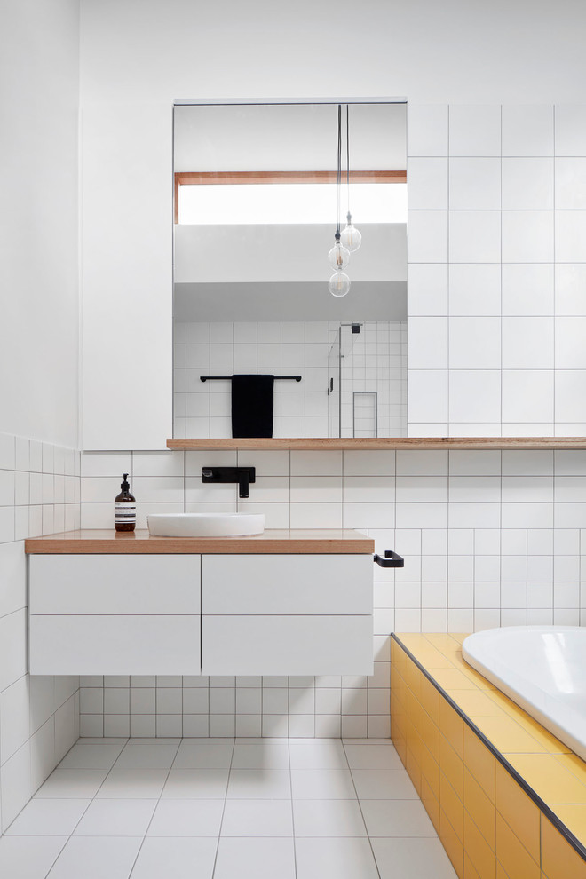 Inspiration for a mid-sized contemporary bathroom in Melbourne with white cabinets, a drop-in tub, white tile, ceramic tile, yellow walls, porcelain floors and wood benchtops.