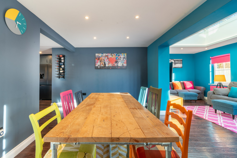 Cette photo montre une salle à manger ouverte sur le salon tendance de taille moyenne avec un mur bleu, parquet foncé, un sol marron et éclairage.