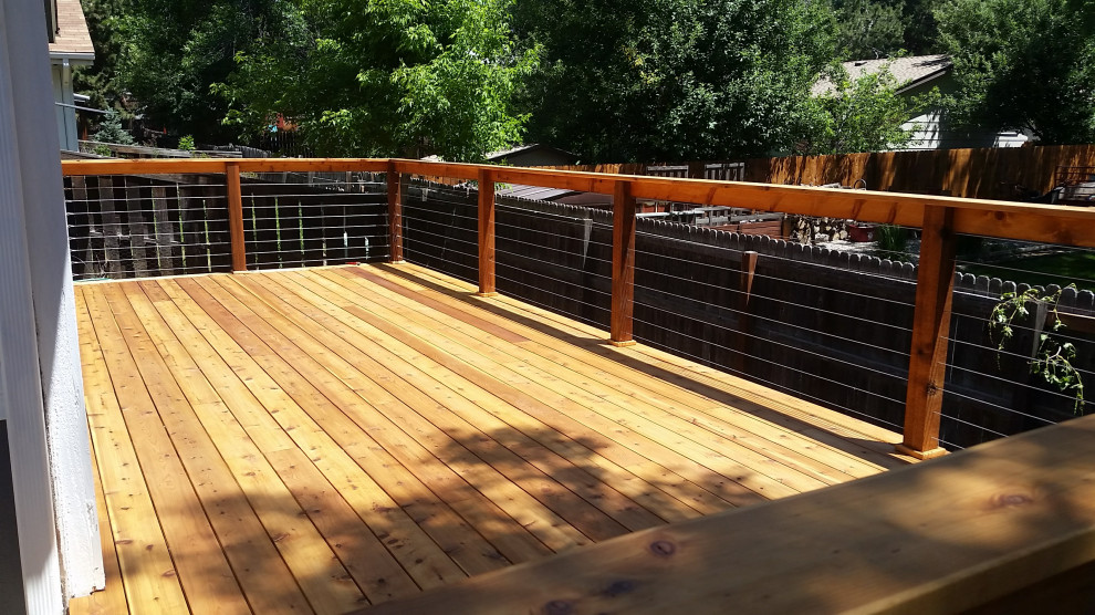 Mid-sized arts and crafts backyard and ground level deck in Denver with with skirting, no cover and cable railing.