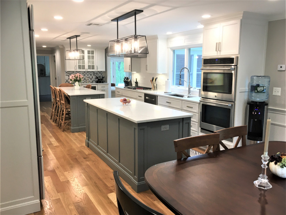 Eat-in kitchen - large transitional galley light wood floor and brown floor eat-in kitchen idea in Boston with an undermount sink, shaker cabinets, white cabinets, quartz countertops, white backsplash, subway tile backsplash, stainless steel appliances, two islands and white countertops