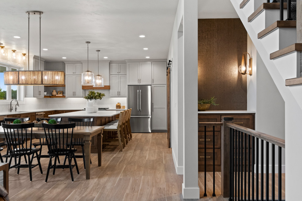 Large transitional l-shaped vinyl floor and brown floor eat-in kitchen photo with an undermount sink, shaker cabinets, brown cabinets, quartz countertops, white backsplash, porcelain backsplash, stainless steel appliances, an island and white countertops