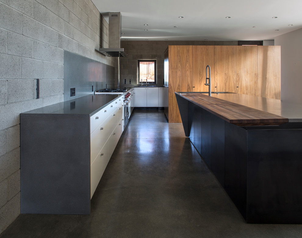 This is an example of a mid-sized modern l-shaped open plan kitchen in Phoenix with an undermount sink, flat-panel cabinets, concrete benchtops, grey splashback, stainless steel appliances, concrete floors, with island, light wood cabinets and stone tile splashback.