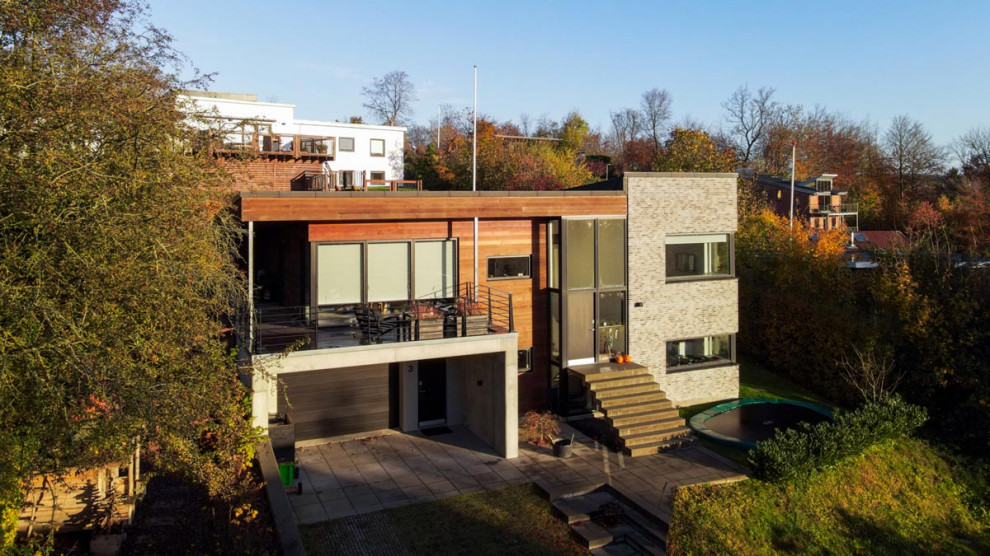 Modelo de fachada de casa gris escandinava de tamaño medio de dos plantas con revestimientos combinados, tejado plano y techo verde