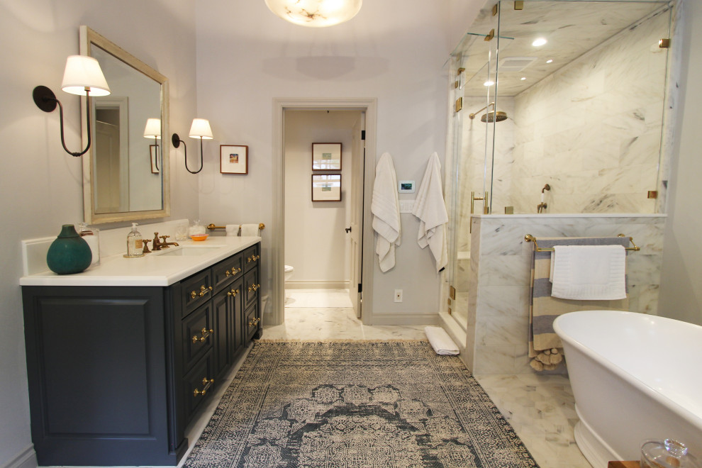 This is an example of an expansive transitional master bathroom in Los Angeles with raised-panel cabinets, blue cabinets, a freestanding tub, an alcove shower, a two-piece toilet, white tile, porcelain tile, white walls, marble floors, an undermount sink, concrete benchtops, white floor, a hinged shower door, grey benchtops, a niche, a single vanity, a built-in vanity, vaulted and planked wall panelling.