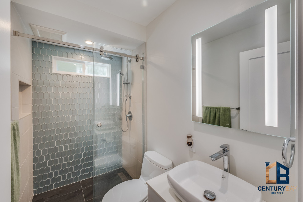 Photo of a traditional bathroom in San Francisco with flat-panel cabinets, brown cabinets, an alcove shower, a two-piece toilet, blue tile, porcelain tile, grey walls, porcelain floors, an integrated sink, engineered quartz benchtops, grey floor, a hinged shower door, white benchtops, a double vanity and a floating vanity.