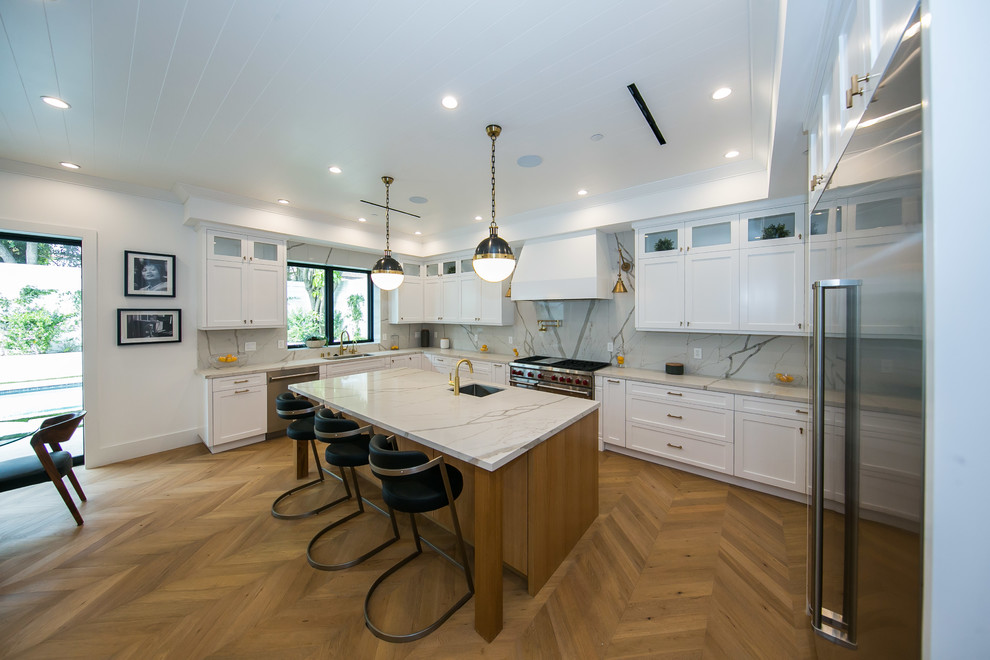 Design ideas for a large modern u-shaped eat-in kitchen in Los Angeles with a drop-in sink, raised-panel cabinets, white cabinets, granite benchtops, white splashback, granite splashback, stainless steel appliances, porcelain floors, with island, beige floor, white benchtop and wood.