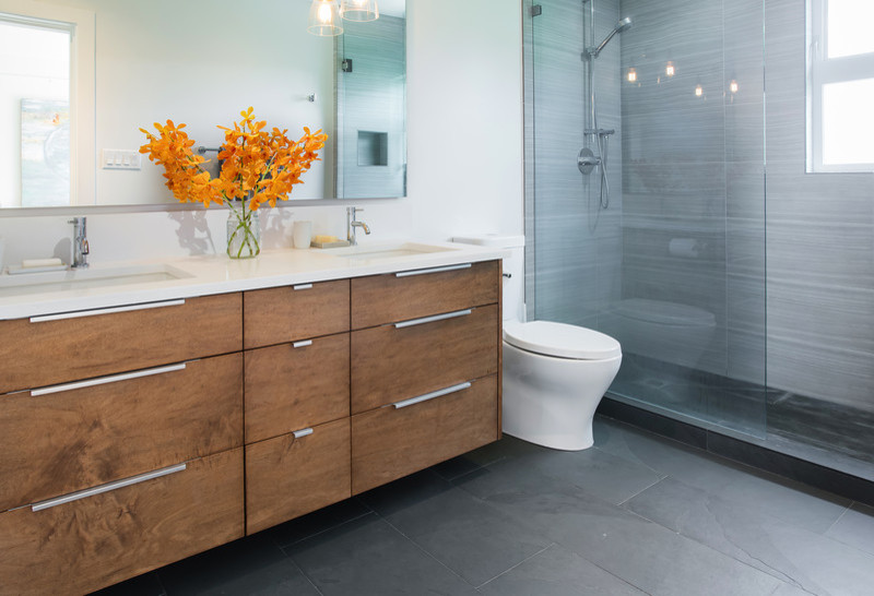 This is an example of a mid-sized contemporary bathroom in Vancouver with an undermount sink, flat-panel cabinets, medium wood cabinets, engineered quartz benchtops, an open shower, a one-piece toilet, beige tile, stone tile, white walls and slate floors.