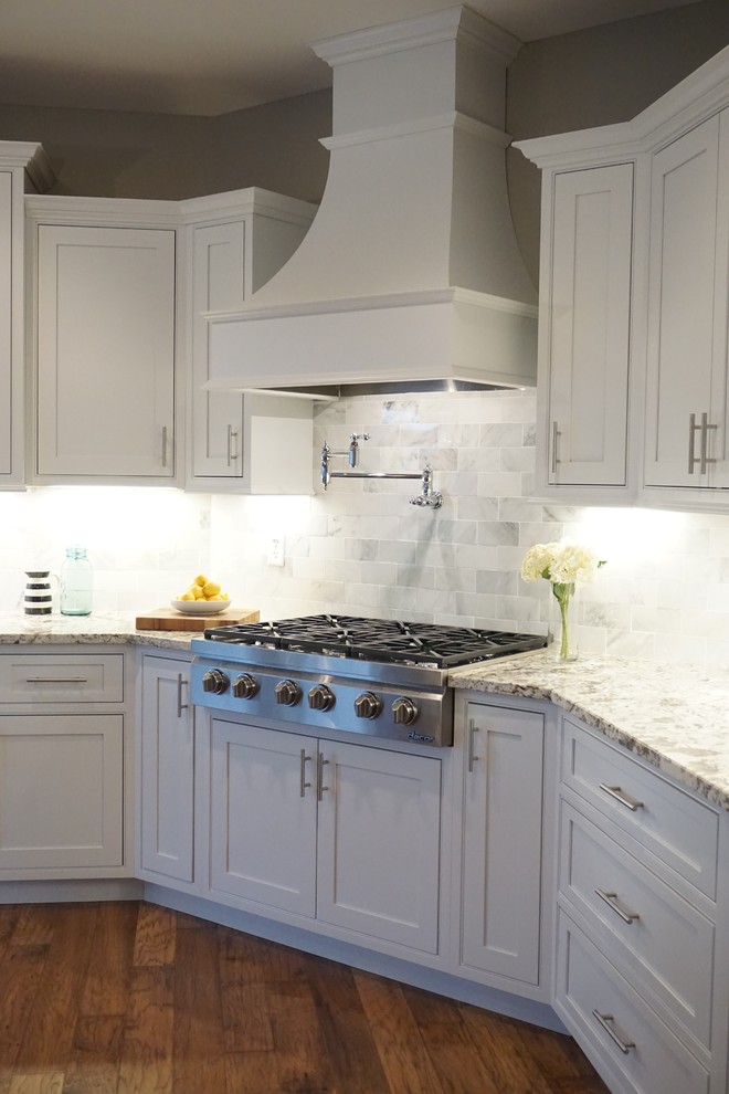 Photo of a traditional eat-in kitchen in St Louis with a farmhouse sink, white cabinets, granite benchtops, white splashback, subway tile splashback, panelled appliances and light hardwood floors.