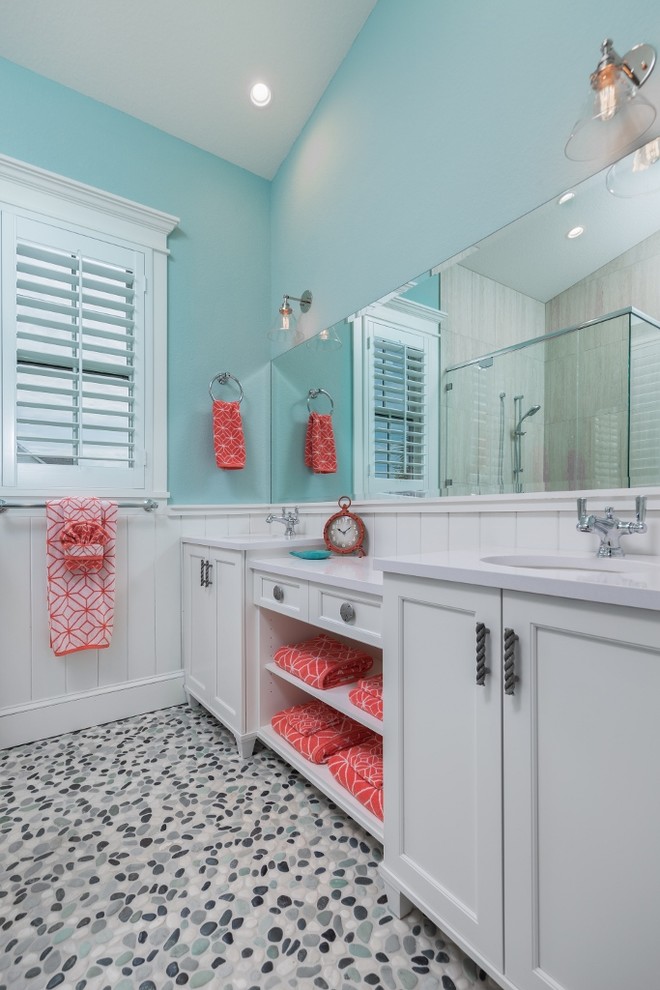 Mid-sized beach style 3/4 bathroom in Tampa with raised-panel cabinets, white cabinets, a corner tub, an open shower, a one-piece toilet, white tile, stone slab, blue walls, pebble tile floors, a drop-in sink and solid surface benchtops.