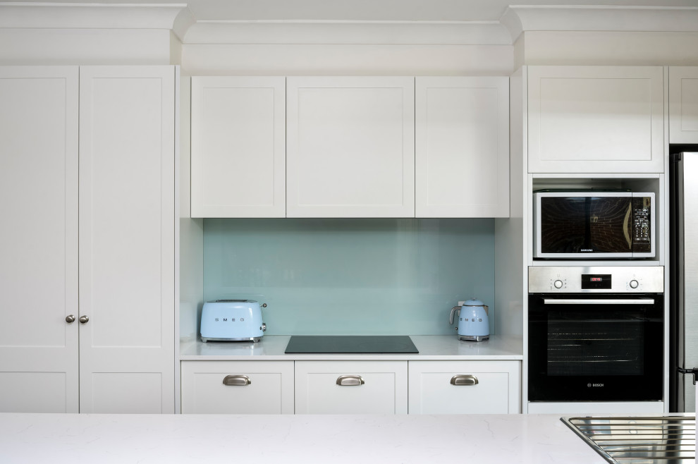 Design ideas for a mid-sized traditional galley eat-in kitchen in Newcastle - Maitland with a drop-in sink, shaker cabinets, white cabinets, quartz benchtops, blue splashback, glass sheet splashback, stainless steel appliances, porcelain floors, a peninsula, brown floor and white benchtop.