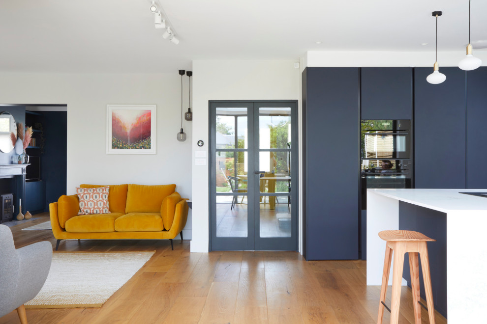 Cette photo montre une cuisine ouverte tendance de taille moyenne avec un placard à porte plane, des portes de placard bleues, un plan de travail en quartz, un électroménager noir, un sol en bois brun et un plan de travail jaune.