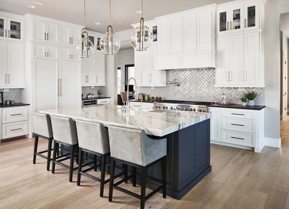 Transitional l-shaped open plan kitchen in Other with a farmhouse sink, shaker cabinets, white cabinets, subway tile splashback, panelled appliances, medium hardwood floors, with island, brown floor and black benchtop.