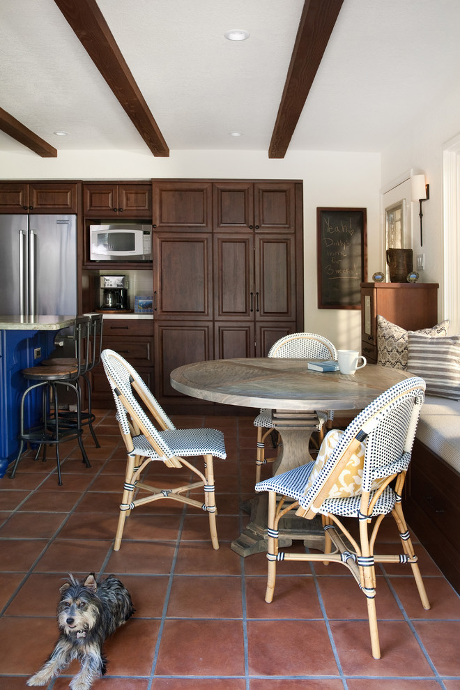 This is an example of a large mediterranean l-shaped eat-in kitchen in Santa Barbara with raised-panel cabinets, dark wood cabinets, stainless steel appliances, terra-cotta floors and with island.