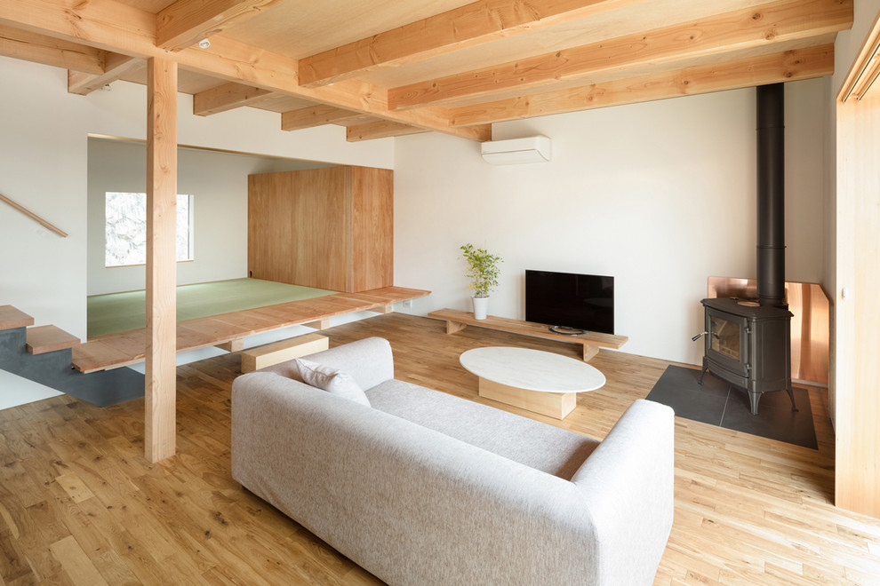This is an example of an asian open concept living room in Osaka with white walls, medium hardwood floors, a freestanding tv and brown floor.