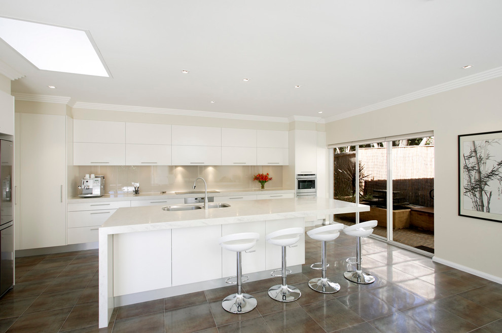 Contemporary l-shaped eat-in kitchen in Sydney with an undermount sink, flat-panel cabinets, white cabinets, glass sheet splashback, beige splashback and stainless steel appliances.