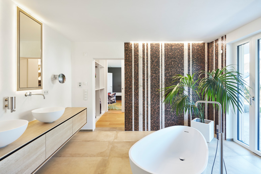 This is an example of a large modern bathroom in Stuttgart with flat-panel cabinets, medium wood cabinets, a freestanding tub, mosaic tile, white walls, a vessel sink, wood benchtops and beige floor.