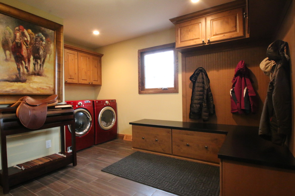 Photo of a mid-sized traditional l-shaped utility room in Milwaukee with a drop-in sink, raised-panel cabinets, medium wood cabinets, granite benchtops, yellow walls, porcelain floors, a side-by-side washer and dryer and brown floor.