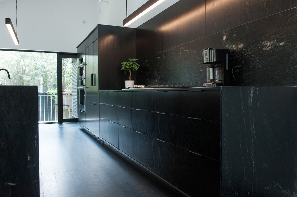 Design ideas for a mid-sized modern galley eat-in kitchen in Houston with an undermount sink, flat-panel cabinets, black cabinets, soapstone benchtops, black splashback, stone slab splashback, panelled appliances, dark hardwood floors, multiple islands, black floor and black benchtop.
