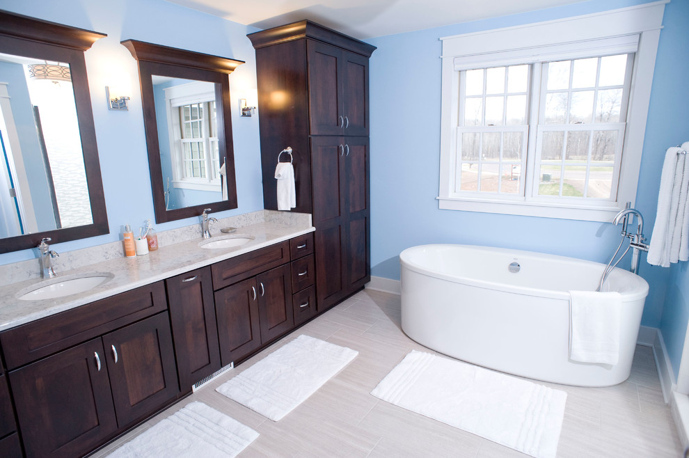 Photo of a large traditional master bathroom in Other with recessed-panel cabinets, dark wood cabinets, a freestanding tub, an alcove shower, white tile, blue walls, porcelain floors, an undermount sink and granite benchtops.