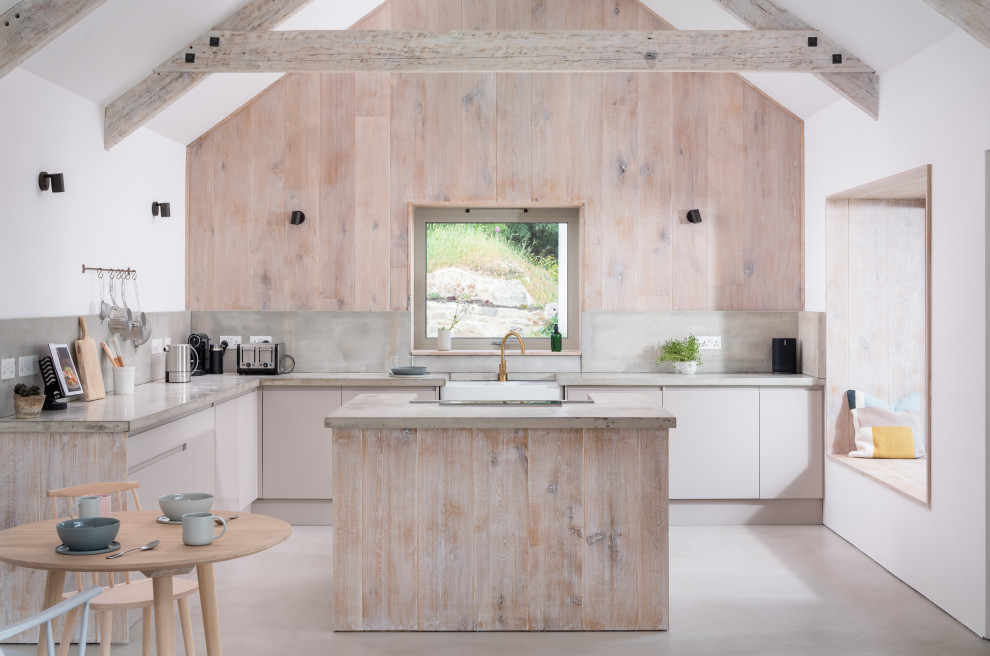 Medium sized rural l-shaped open plan kitchen in Cornwall with a belfast sink, flat-panel cabinets, beige cabinets, concrete worktops, concrete flooring, an island and beige floors.